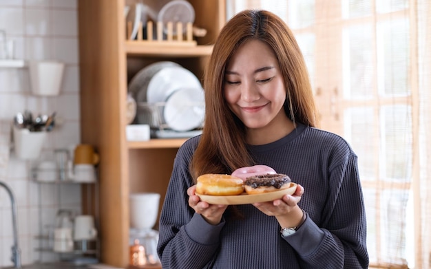 Porträtbild einer schönen jungen asiatischen Frau, die zu Hause einen Teller Donuts in der Küche hält