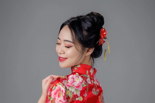 Porträtfotografie: lächelnde asiatische chinesische Frau im traditionellen Cheongsam Qipao-Kleid auf weißem oder grauem Hintergrund chinesisches Neujahrsfestkonzept