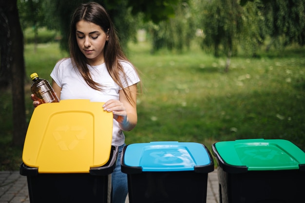 Porträtfrau, die im Freien leere Plastikwasserflasche in Recyclingbehälter wirft