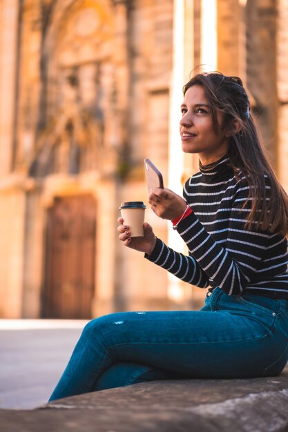 Porträtfrau, die Kaffee im Park genießt, während sie Handy verwendet