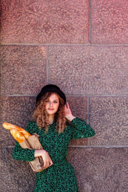 Porträtfrau im französischen Stil mit Baguette in der Hand gekleidet. Französischer Stil von Paris. Nahaufnahme der Französin in stilvoller Kleidung, die frische Baguettes hält und lächelt. Platz für eine Inschrift oder ein Logo