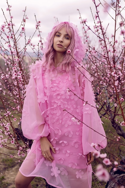 Porträtfrau in einem rosa Kleid mit Blumen steht neben einem Pfirsichbaum