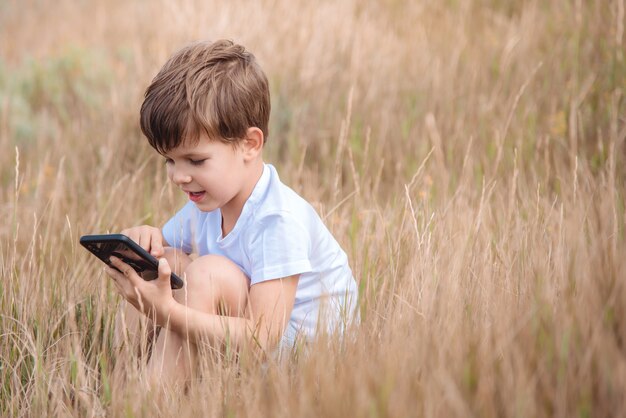 Porträtjunge sitzt auf dem Rasen mit Telefon