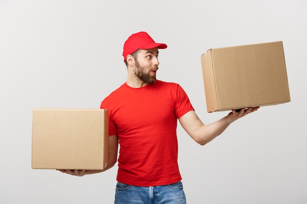 Porträtlieferant in der Kappe mit dem roten T-Shirt, das als Kurier oder Händler arbeitet, der zwei leere Pappkartons hält.