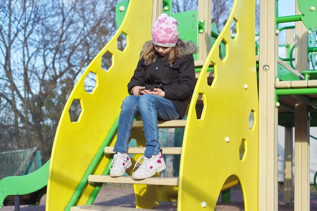 Porträtmädchen im Freien mit Smartphone am Spielplatz