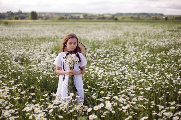 Porträtmädchen in einem weißen Kleid mit Hut im Blumenfeld