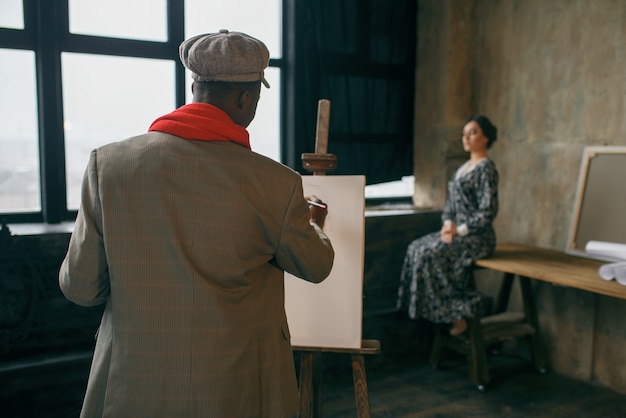 Porträtmaler mit Pinsel zeichnet weibliches Modell. Männlicher Künstler, der an seinem Arbeitsplatz steht, kreativer Meister an der Staffelei in der Werkstatt
