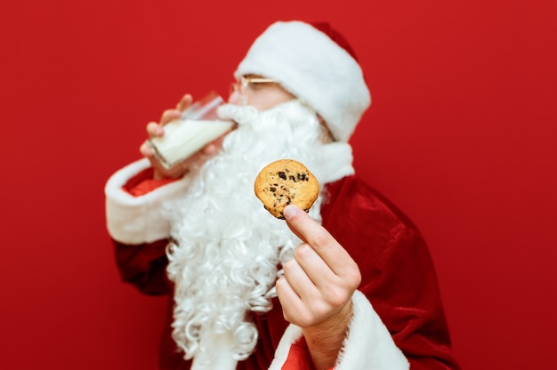 Porträtmann verkleidet als weihnachtsmann, der glas milch und teller mit schokoladenplätzchen hält