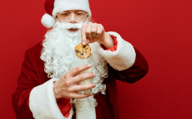 Porträtmann verkleidet als weihnachtsmann, der glas milch und teller mit schokoladenplätzchen hält