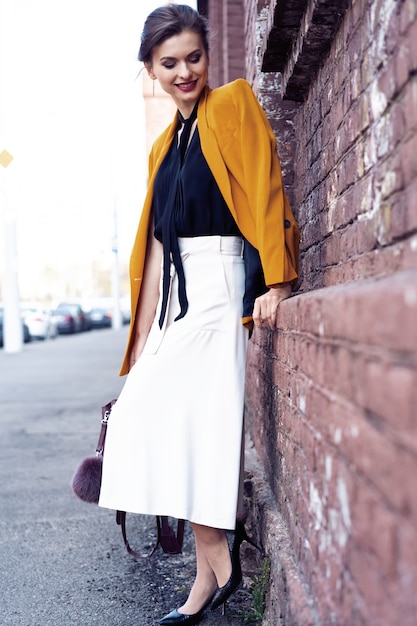 Porträtmodefrau, die auf Straße geht. Sie trägt eine gelbe Jacke und lächelt zur Seite.