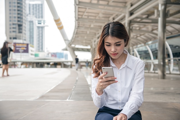 Porträts des schönen asiatischen Frauenblickvertrauens hält Mobiltelefon.