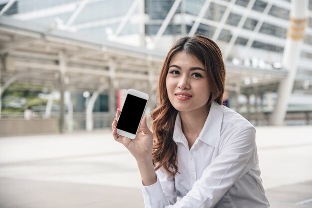 Porträts des schönen asiatischen Frauenblickvertrauens hält Mobiltelefon.