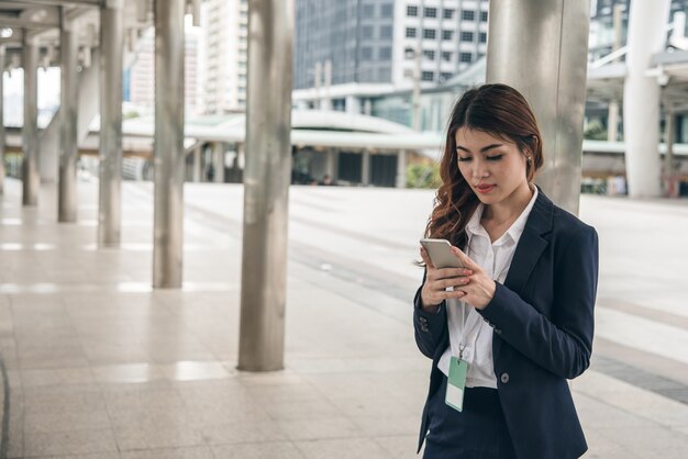 Porträts des schönen asiatischen Frauenblickvertrauens hält Mobiltelefon.