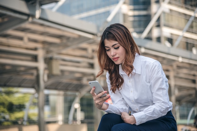 Porträts des schönen asiatischen Frauenblickvertrauens hält Mobiltelefon.