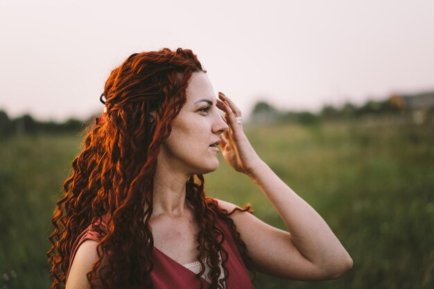 Porträts einer charmanten rothaarigen Frau mit einem süßen Gesicht Mädchen, das bei Sonnenuntergang für die Kamera auf dem Feld posiert