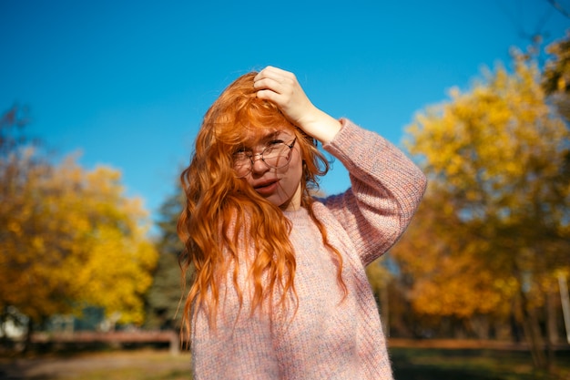 Porträts eines charmanten rothaarigen Mädchens mit einem niedlichen Gesicht. Mädchen, das im Herbstpark in einem Pullover und in einem korallenfarbenen Rock aufwirft. Das Mädchen hat eine wundervolle Stimmung