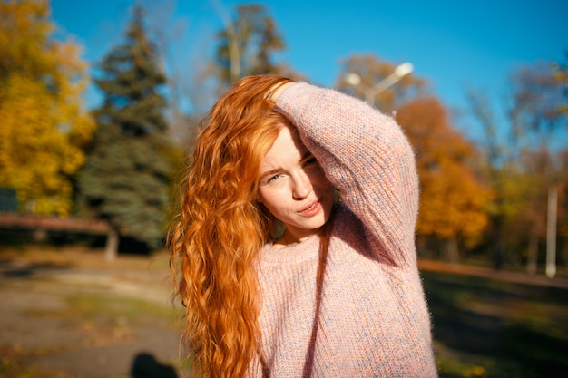 Porträts eines charmanten rothaarigen Mädchens mit einem niedlichen Gesicht. Mädchen, das im Herbstpark in einem Pullover und in einem korallenfarbenen Rock aufwirft. Das Mädchen hat eine wundervolle Stimmung