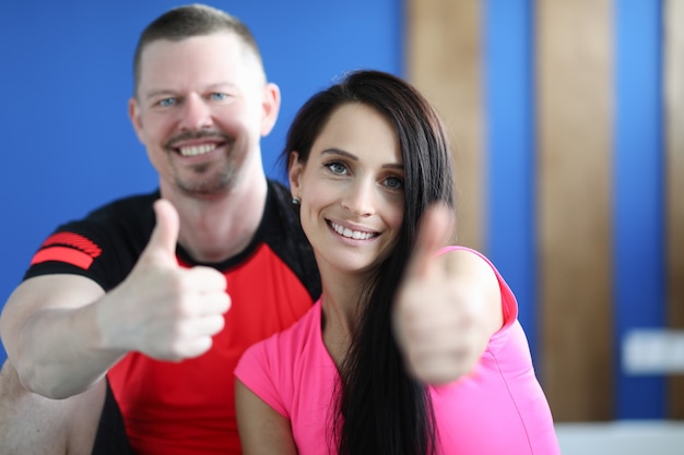 Porträts von lächelndem Mann und Frau im Fitnessstudio und Daumen hoch Geste zeigen
