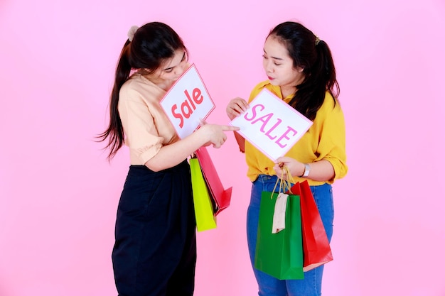 Porträtstudio schoss asiatische junge glückliche Käuferin in lässigem Outfit mit bunten Einkaufstüten, die Verkaufsrabatt-Bannerpapier auf rosafarbenem Hintergrund zeigen.