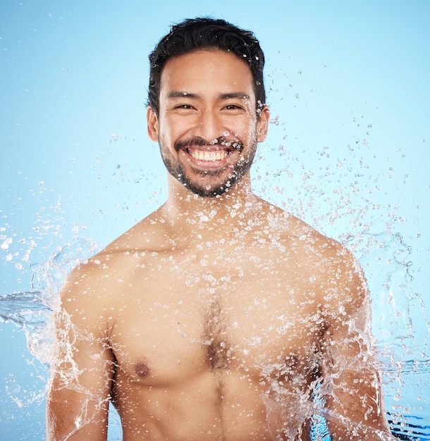 Porträtwasser und Dusche mit einem Mannmodell im Studio auf blauem Hintergrund für Hygiene oder Flüssigkeitszufuhr Gesichtsschönheit und Hautpflege mit einem hübschen jungen Mann, der von einem Wasserspritzer im Badezimmer nass ist