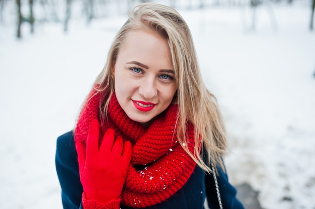 Portrai des blonden Mädchens im roten Schal und im Mantel am Wintertag.