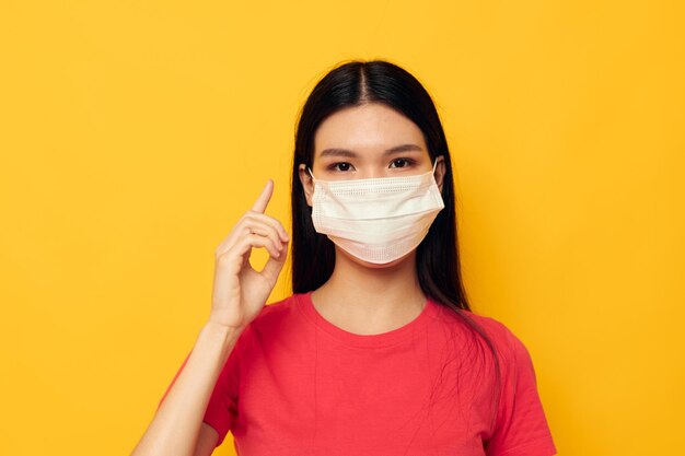 Portrait asiatische schöne junge Frau im roten T-Shirt medizinischer Maskenschutz gelber Hintergrund unverändert