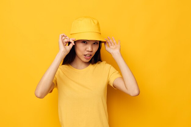 Portrait Asiatische schöne junge Frau in einem gelben T-Shirt und Hut, die Emotionen aufwirft Lifestyle unverändert