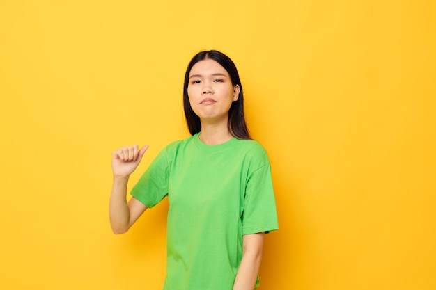 Portrait asiatische schöne junge Frau in grünen T-Shirts Gesten mit seinen Händen Emotionen gelben Hintergrund unverändert
