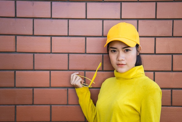 Portrait asiatisches Hipster-Mädchen auf Backsteinmauerhintergrund, sie trägt einen gelben Ton-GanzkörperLifestyle der thailändischen Bevölkerung