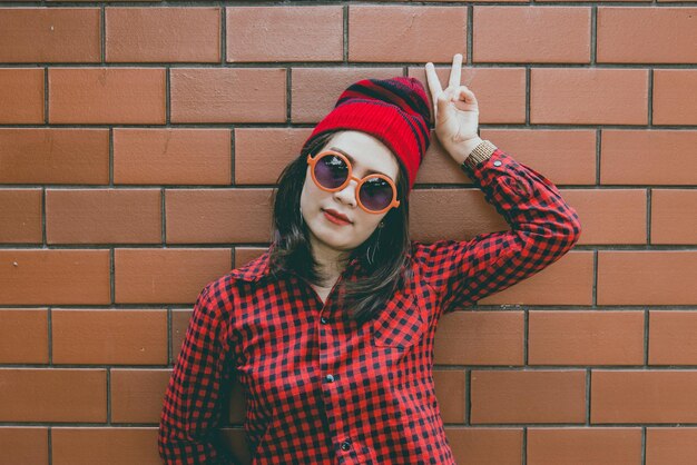 Portrait asiatisches Hipster-Mädchen auf Backsteinmauerhintergrund, sie trägt einen roten Hut im Vintage-Stil, Modekonzept, Thailand-Leute