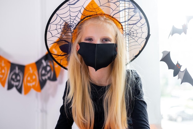 Portrait blondes Mädchen im Hexenkostüm mit Gesichtsmasken, die sich auf Halloween vorbereiten und vor COVID19 schützen
