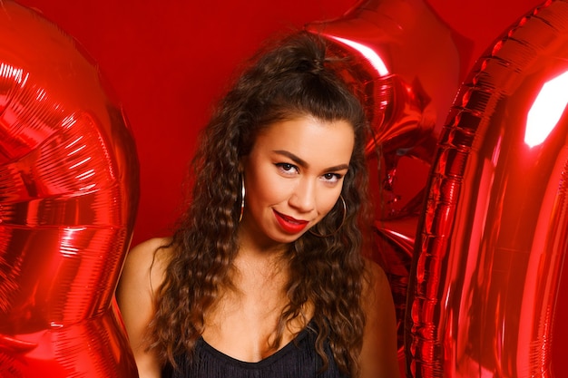 Portrait der glücklichen jährigen Frau auf rotem Hintergrund mit roten Luftballons ein schönes Mädchen der kaukasischen ...