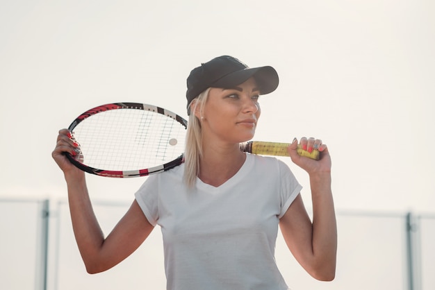 Portrait der jungen schönen Frau mit Schläger für Tennis auf einem Gericht