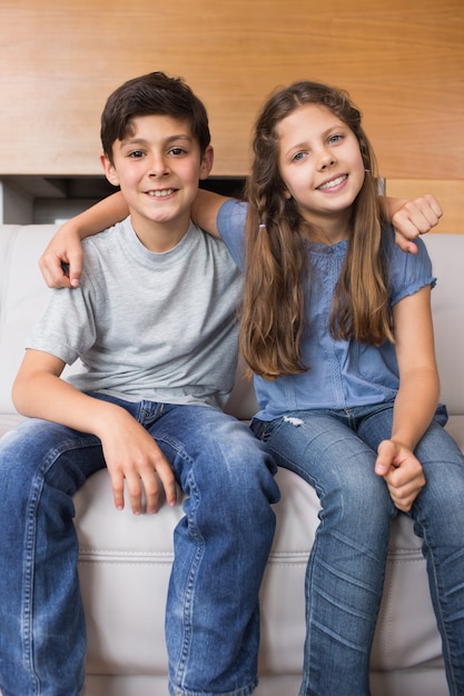 Portrait der lächelnden kleinen Geschwister, die im Wohnzimmer sitzen