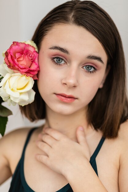 Portrait der schönen dunkelhaarigen Frau mit Blumen. Modefoto, Hübsches kleines Mädchen mit rosa Rose