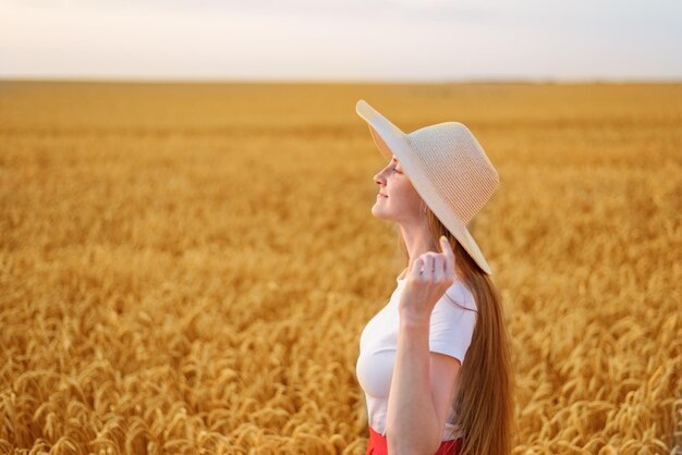 Portrait der schönen jungen Frau im Hut auf Weizenfeldhintergrund Seitenansicht
