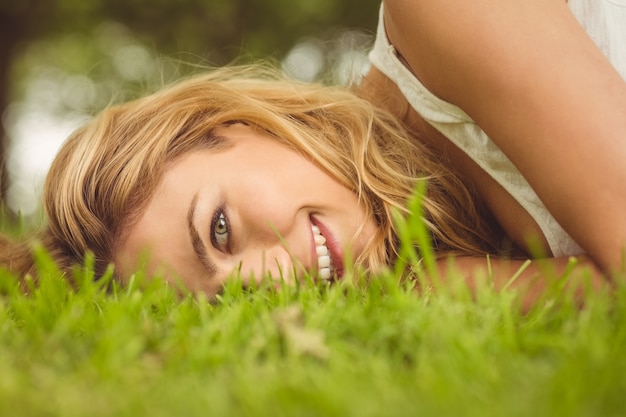 Portrait der schönen lächelnden Frau, die auf Gras liegt