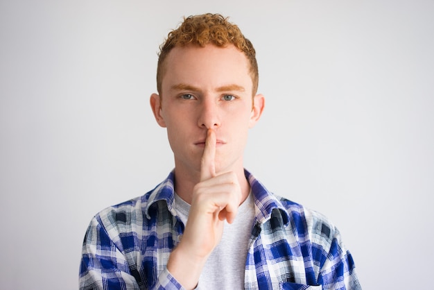 Foto portrait des ernsten jungen mannes mit dem finger auf lippen