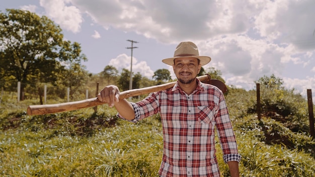 Portrait des jungen Mannes im Freizeithemd, das seine Hacke in der Farm hält Farm-Tool Lateinischer Mann