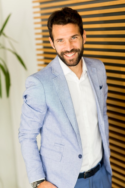 Portrait des stattlichen jungen Geschäftsmannes, der gegen Wand steht