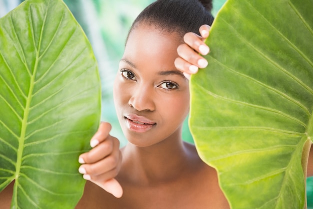 Portrait einer hübschen Frau, die durch Blätter auf einem greenness Hintergrund schaut