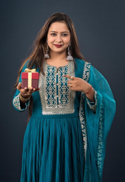 Portrait einer jungen glücklich lächelnden Frau Mädchen, das Geschenkbox auf einem grauen Hintergrund hält