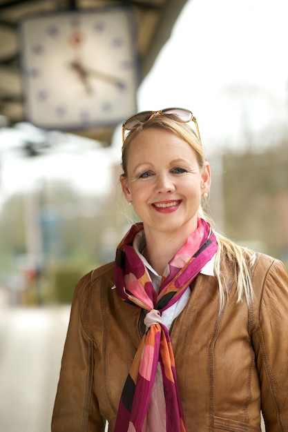 Portrait einer schönen älteren Frau, die unter Bahnstationborduhr lächelt