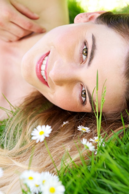 Portrait einer schönen Frau, die im Park mit Blumen liegt