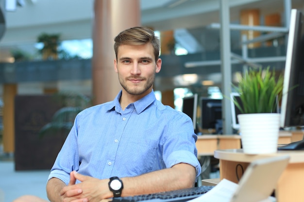 Portrait eines glücklichen Mannes, der am Schreibtisch sitzt und in die Kamera schaut, lächelnd.