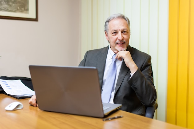 Portrait eines lächelnden älteren Geschäftsmannes, der in seinem Büro sitzt