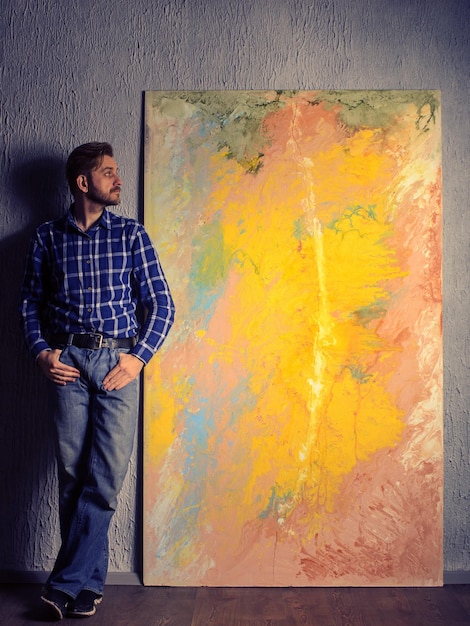 Portrait eines männlichen Künstlers, der neben seiner abstrakten Malerei im Studio steht