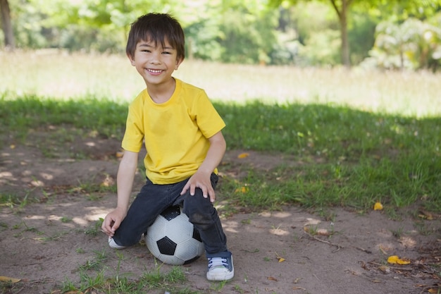 Portrait eines netten Jungen, der auf Fußball am Park sitzt