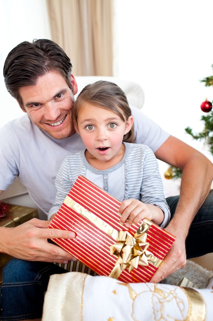 Portrait eines überraschten kleinen Mädchens, das ein Weihnachtsgeschenk anhält