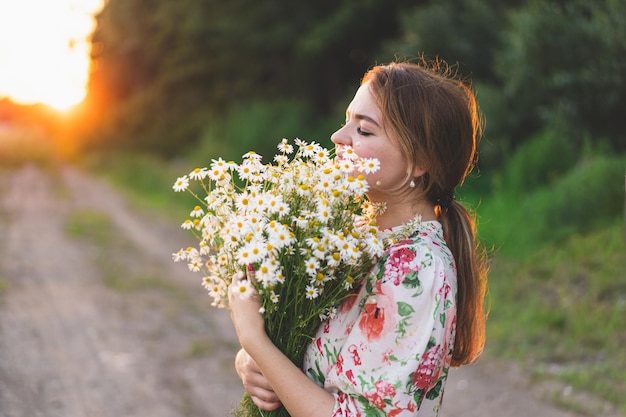 Portrait Frau mit Kamillenblüten bei Sonnenuntergang Leben ohne Allergien frei atmen Frau Spaß im Sommer in der Natur Frau träumt und lächelt vor dem Hintergrund eines Kamillenfeldes